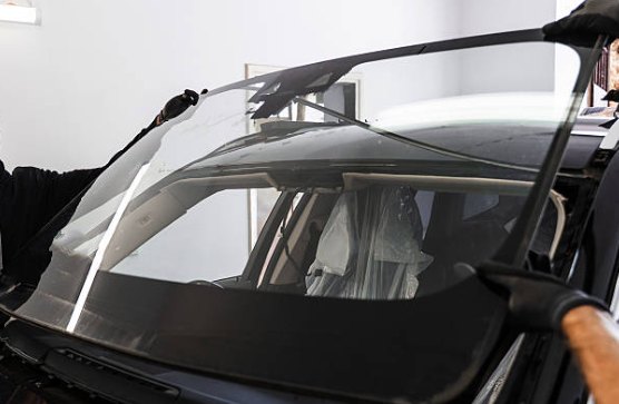Replacement windshield being lowered squarely into the prepared pinch weld of a vehicle